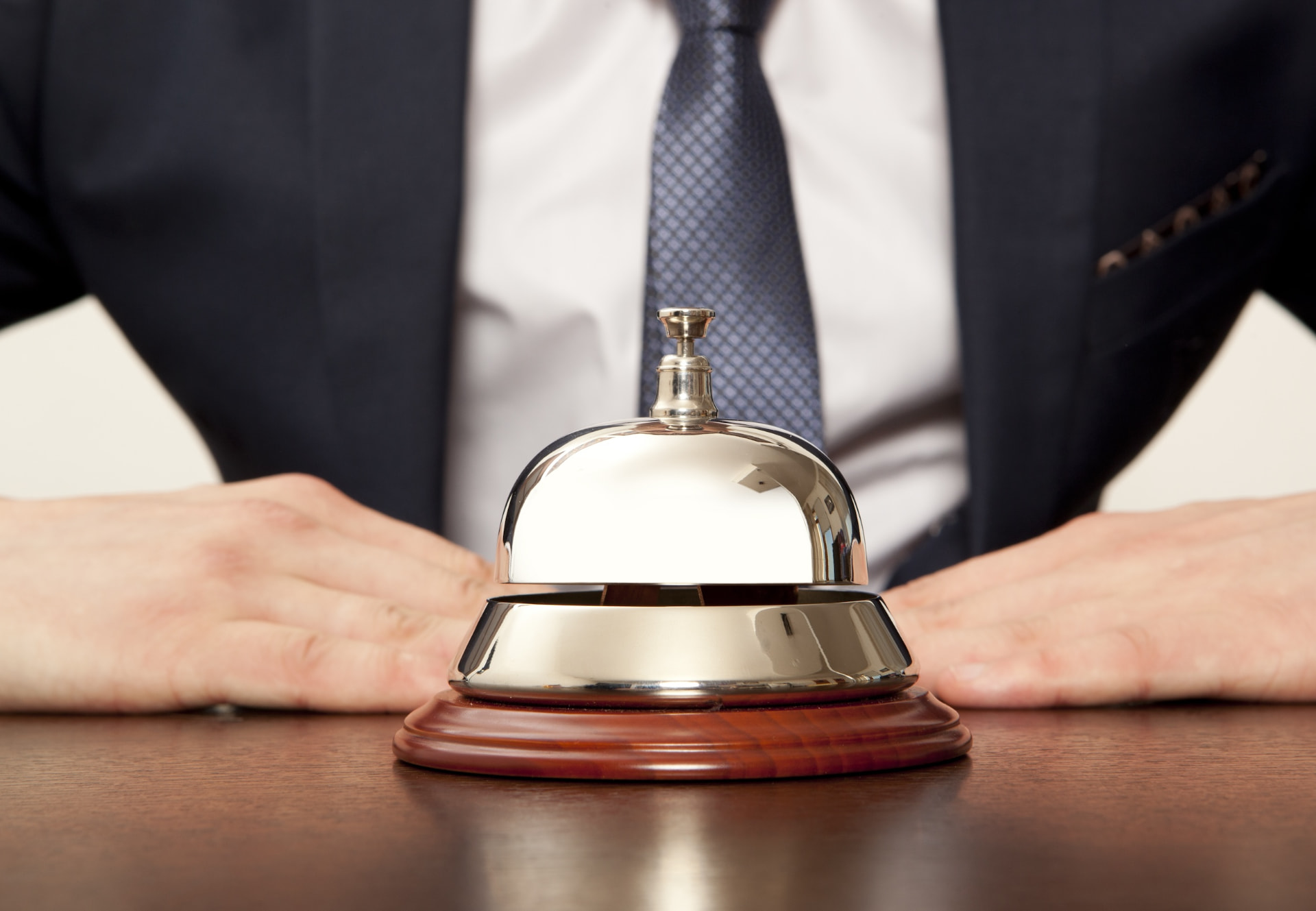 Polished reception bell on a wooden counter with a suited hotel concierge behind it